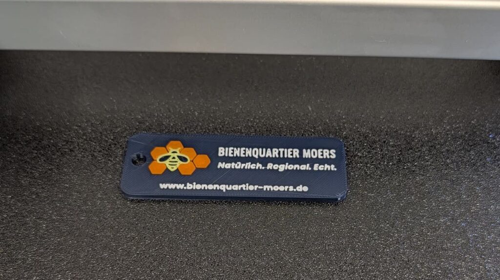 Schlüsselanhänger aus dem 3D-Druck mit Bienenquartier-Moers-Logo auf der Druckplatte